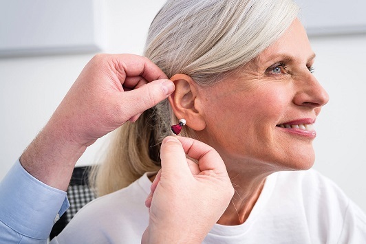 Ältere Frau bekommt ein modernes Hörgerät eingesetzt, Hörhilfe Beratung Hörakustiker.